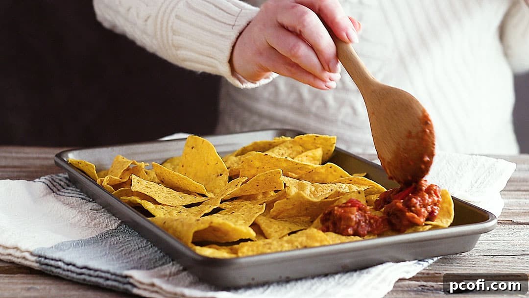 Spooning chili over tortilla chips for nachos recipe.