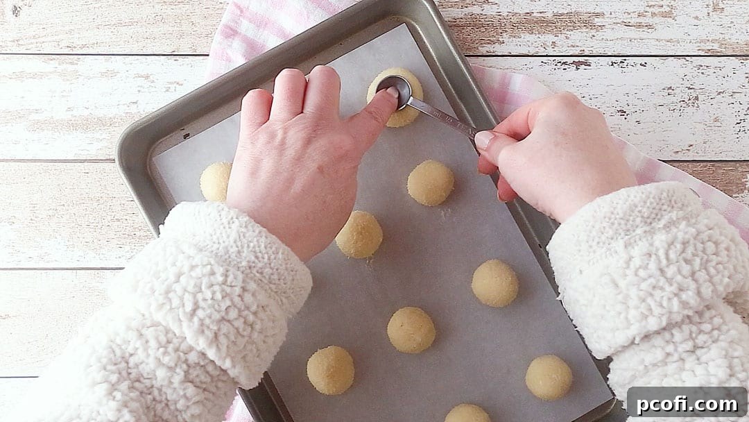 Pressing the back of a measuring spoon into thumbprint cookie dough to make a well for the jam.
