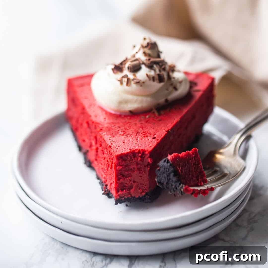 Slice of red velvet cheesecake with Oreo crust, whipped cream, and chocolate shavings.