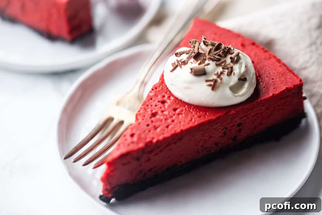 Slice of red velvet cheesecake with Oreo crust, whipped cream, and chocolate shavings.