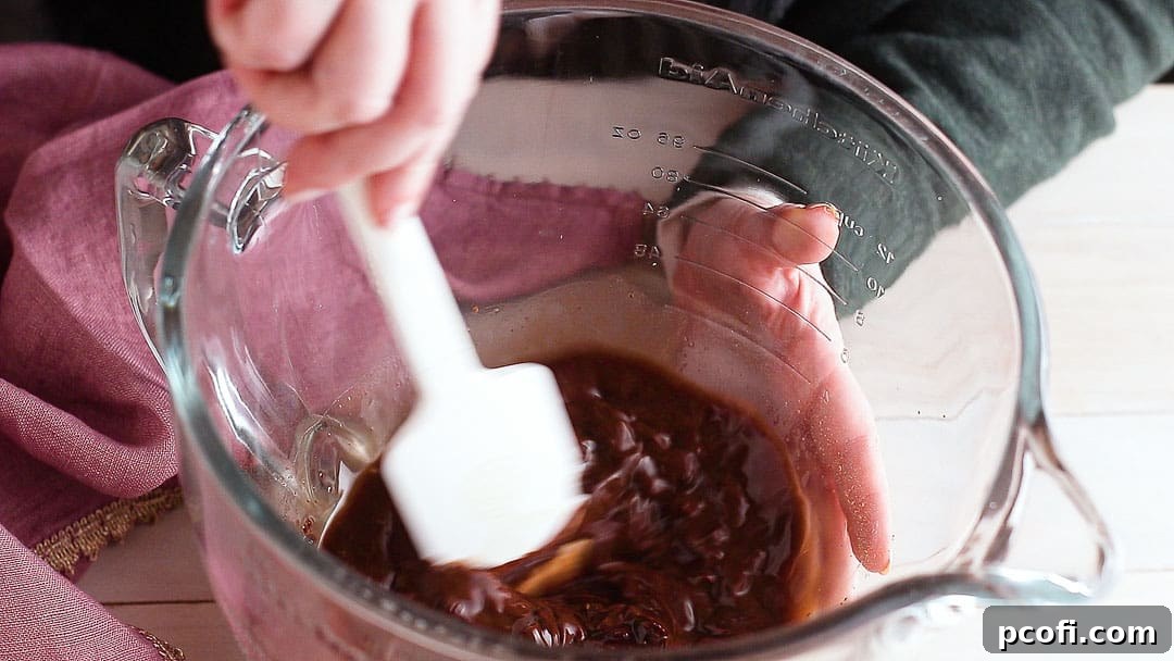 Stirring melted chocolate base ingredients (chocolate, water, cocoa, sugar, salt) together until smooth and glossy in a glass bowl.