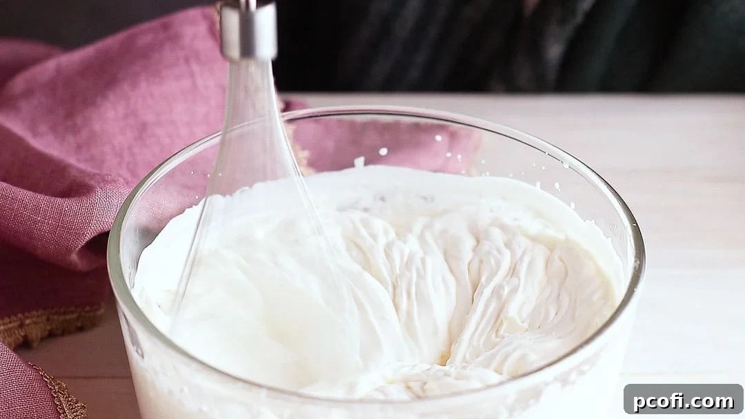 Heavy whipping cream being whipped to stiff peaks in a stand mixer with a whisk attachment, essential for an airy chocolate mousse.
