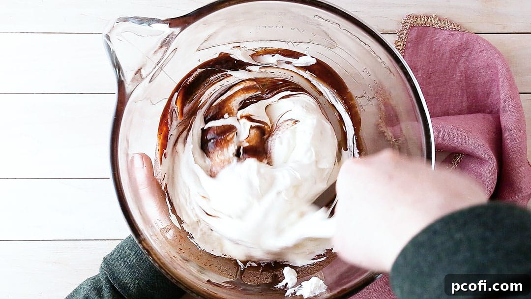 Gently folding stiffly whipped cream into the melted chocolate mixture using a spatula, ensuring the mousse remains light and airy.