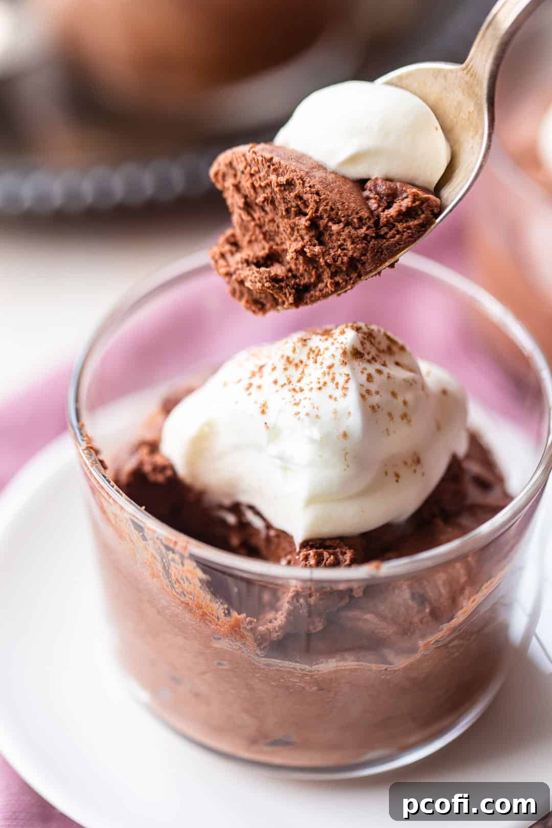 A silver spoon scooping a generous portion of rich, easy chocolate mousse from a glass bowl, showcasing its airy texture.