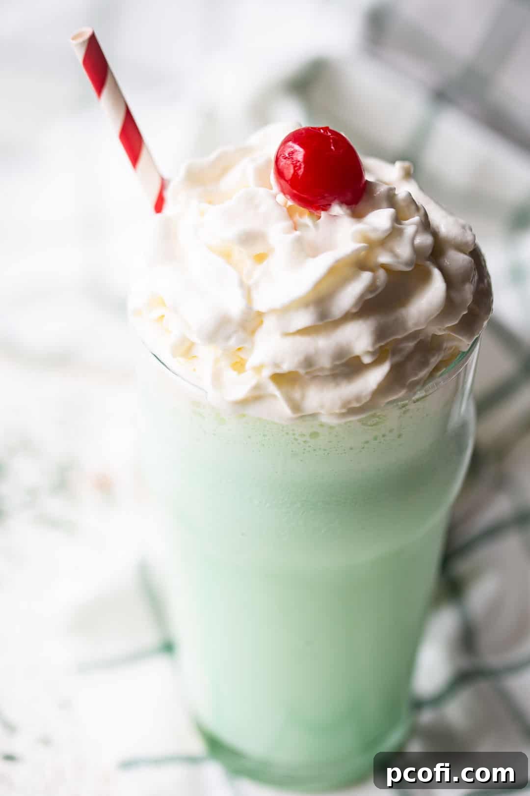 Shamrock shake recipe prepared and served in a glass with whipped cream, with a green plaid napkin in the background.