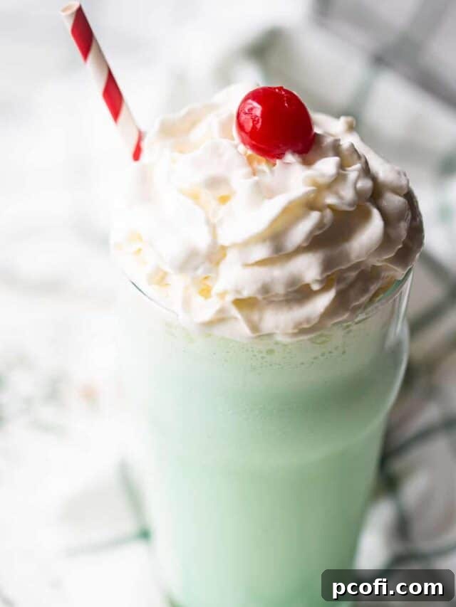 Shamrock shake recipe prepared and served in a glass with whipped cream, with a green plaid napkin in the background.