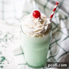 Shamrock shake in a tall glass with whipped cream and a cherry on top.