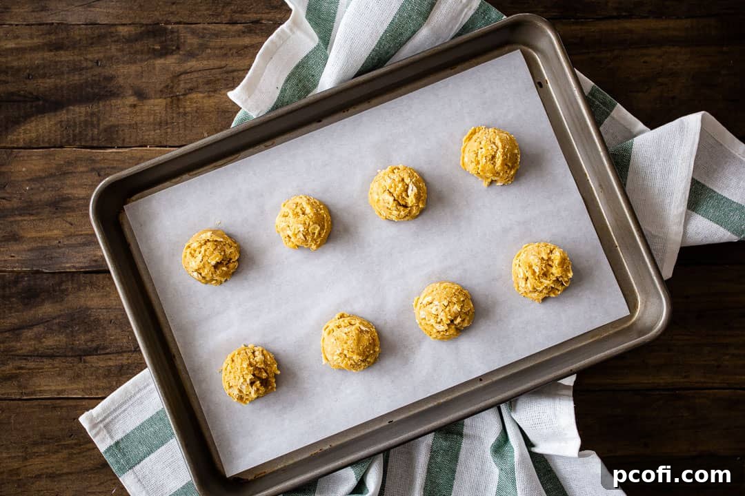 Scooping oatmeal cookie dough onto a parchment-lined baking sheet.