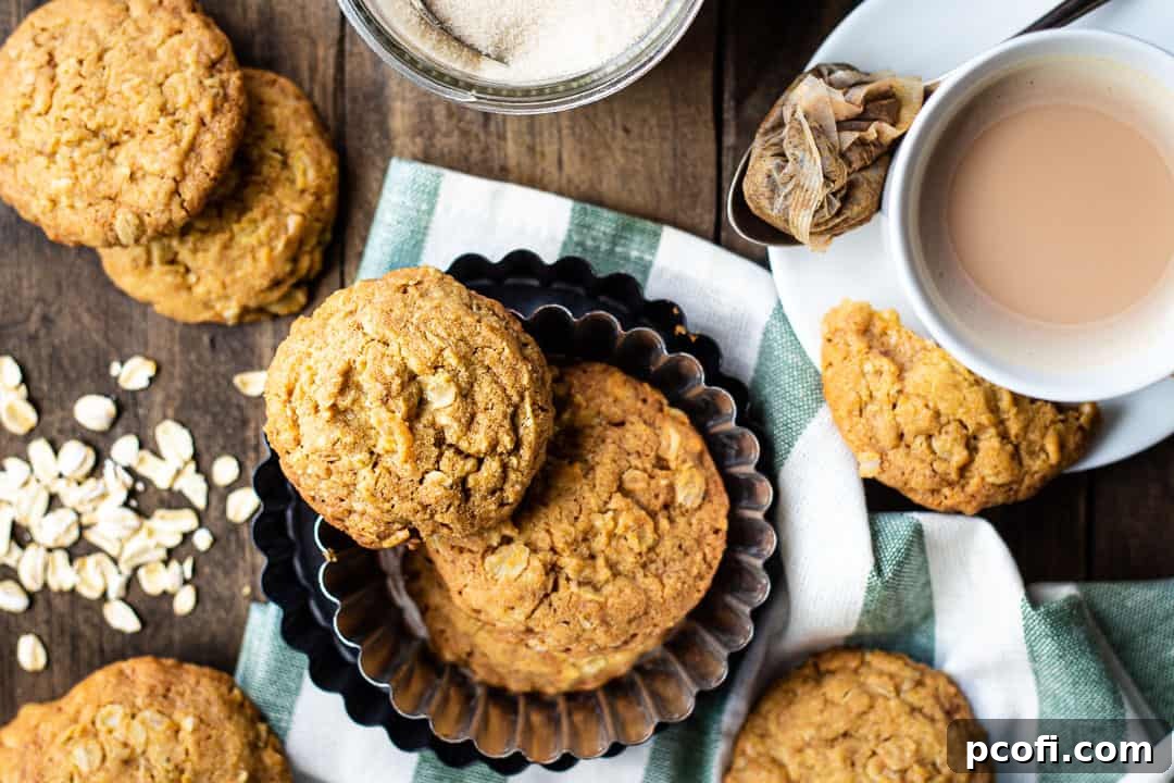 Homemade oatmeal cookies on a wooden tabletop, with a cup of tea and oats.