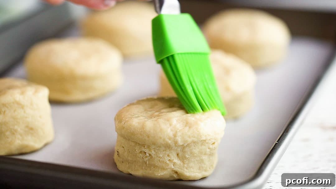 Brushing unbaked scones with egg wash on a parchment-lined baking sheet.