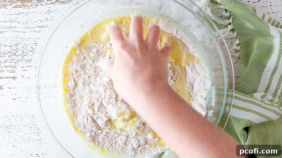 Using clean hands in a 'claw' shape to combine scone ingredients.