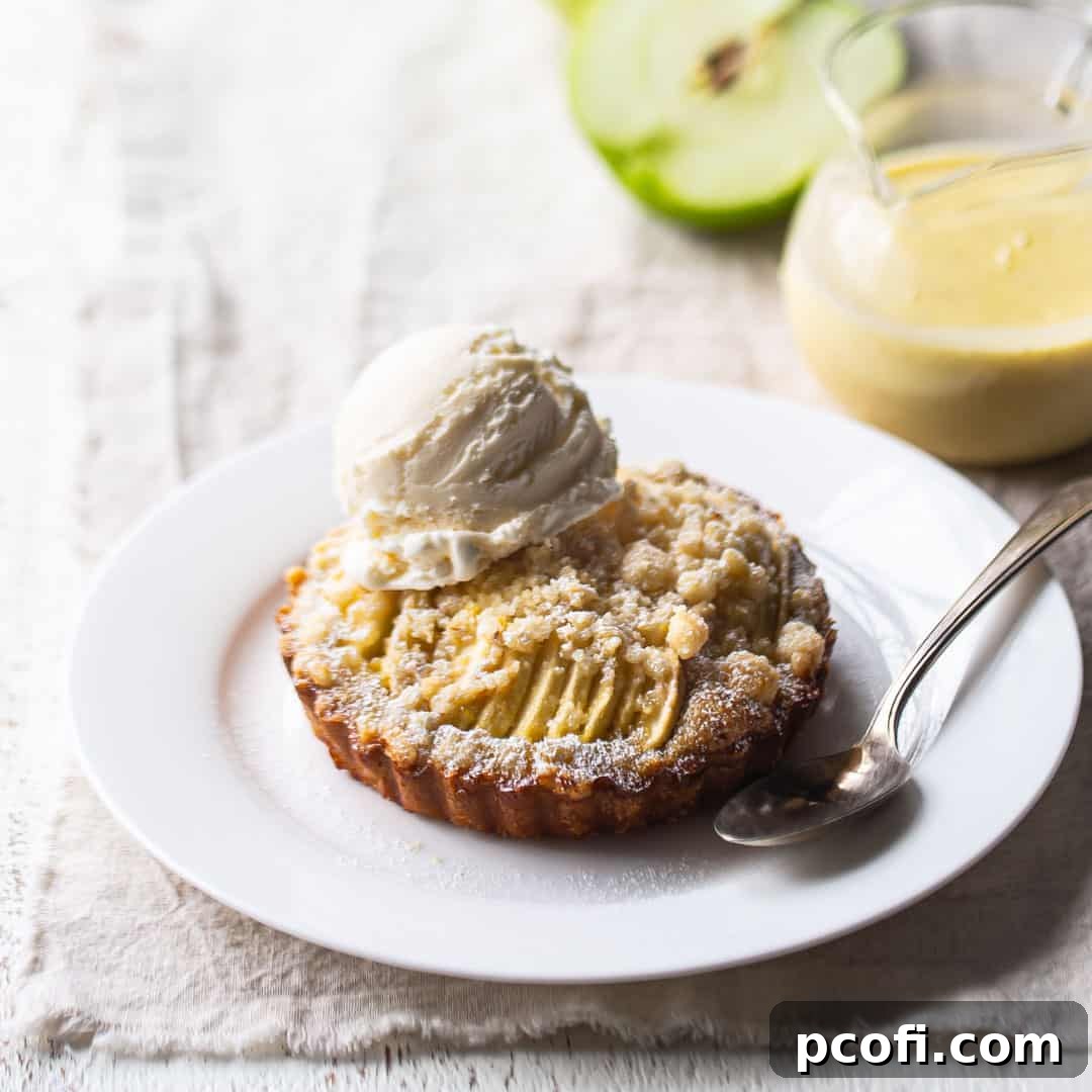 Apple tart with crumb topping on a white plate with a scoop of vanilla ice cream.