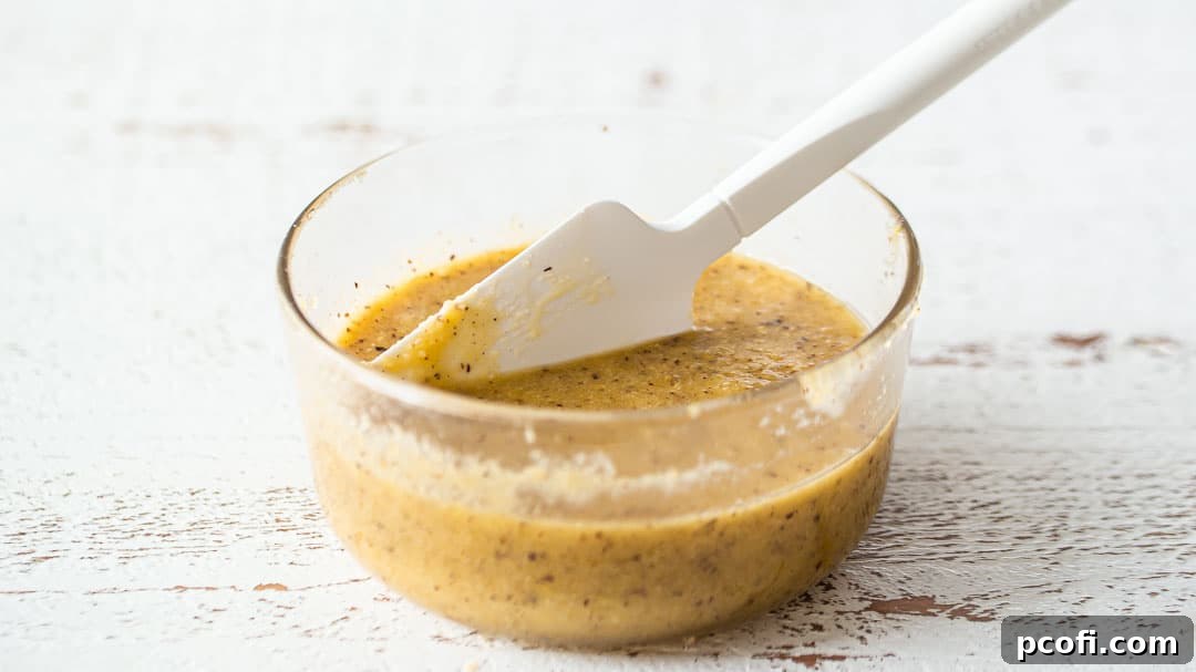 Smooth frangipane filling in a glass bowl, ready to be spread into the tart shells, with a silicone spatula resting in it.