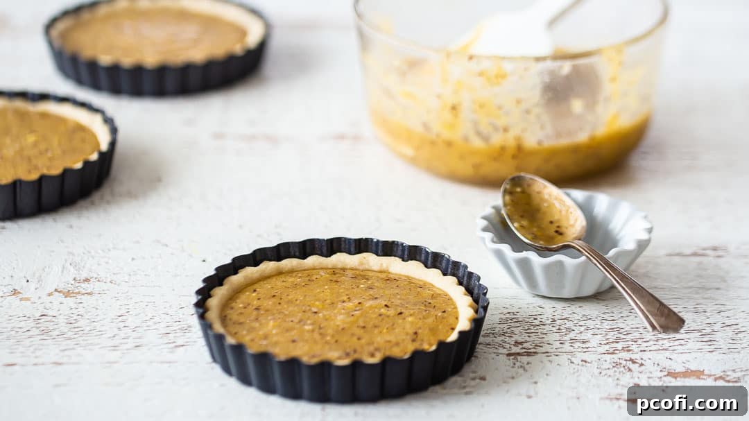 Partially baked mini-tart shells, now elegantly filled with a smooth layer of frangipane, awaiting the apples.