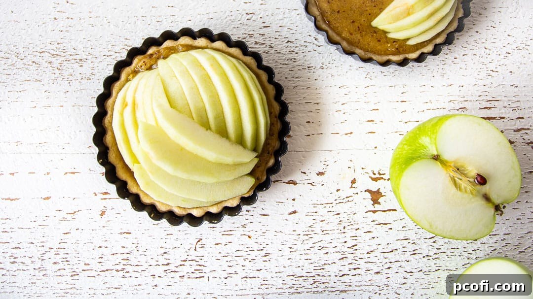 Thinly sliced apples artfully arranged over the frangipane filling in a mini tart shell, ready for the crumb topping.
