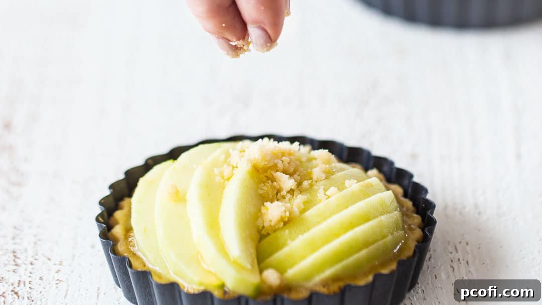 Gently sprinkling buttery crumb topping over unbaked mini apple tarts, ready for baking.