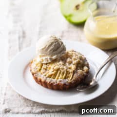 Apple tart with crumb topping on a white plate with a scoop of vanilla ice cream.