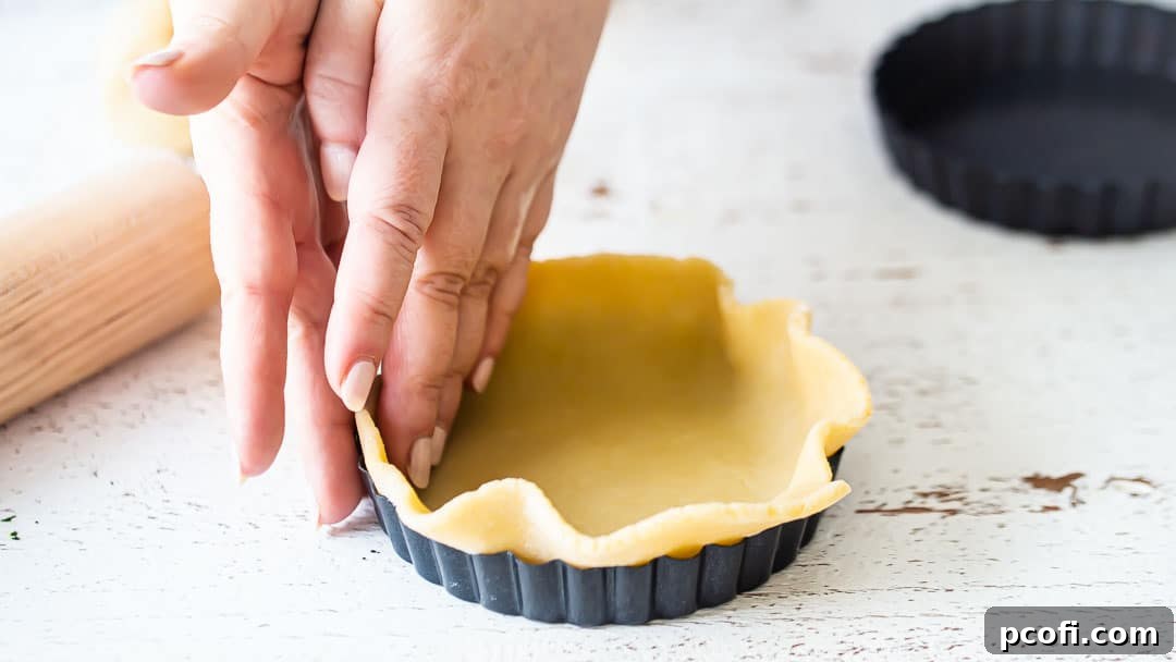 Easing tart dough into a mini tart pan, preparing for the baking process.