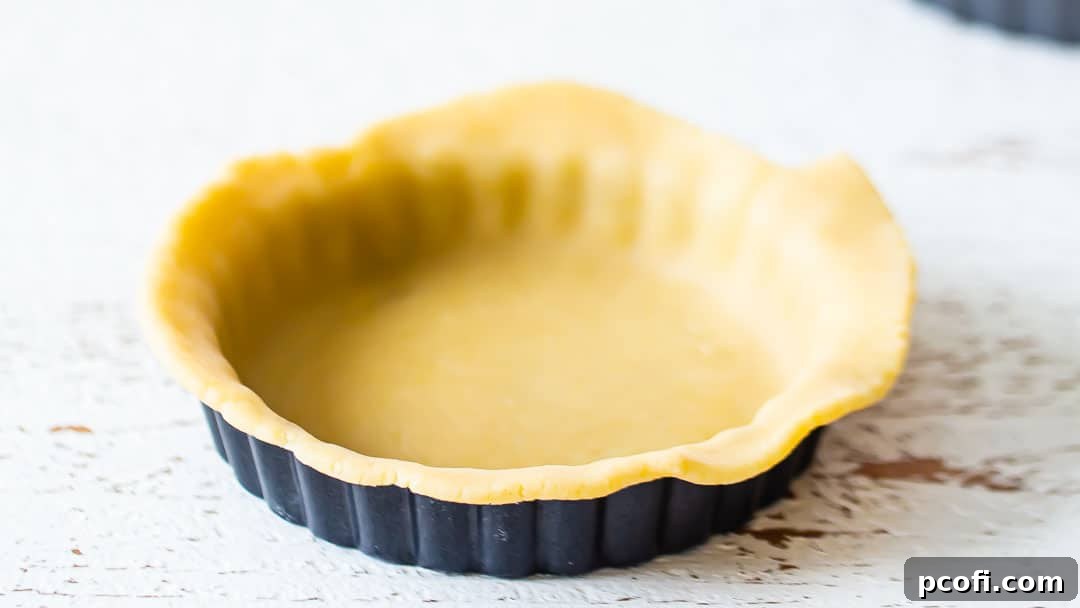 Mini tart pan with tart dough hanging over the sides, ready for trimming.