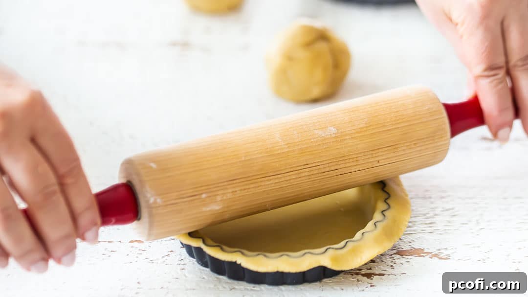 Trimming excess dough from mini tarts with a rolling pin for a clean edge.