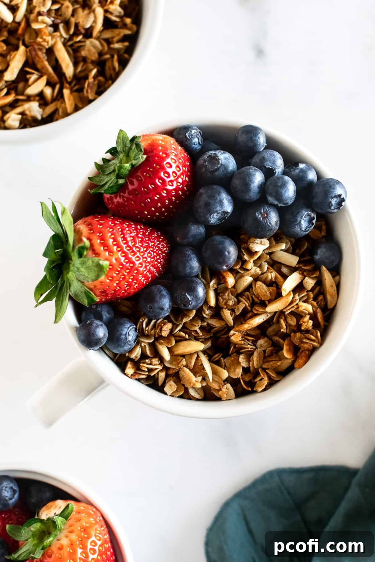 A bowl of homemade granola generously topped with fresh, vibrant strawberries and blueberries, showcasing a healthy and delicious breakfast option.