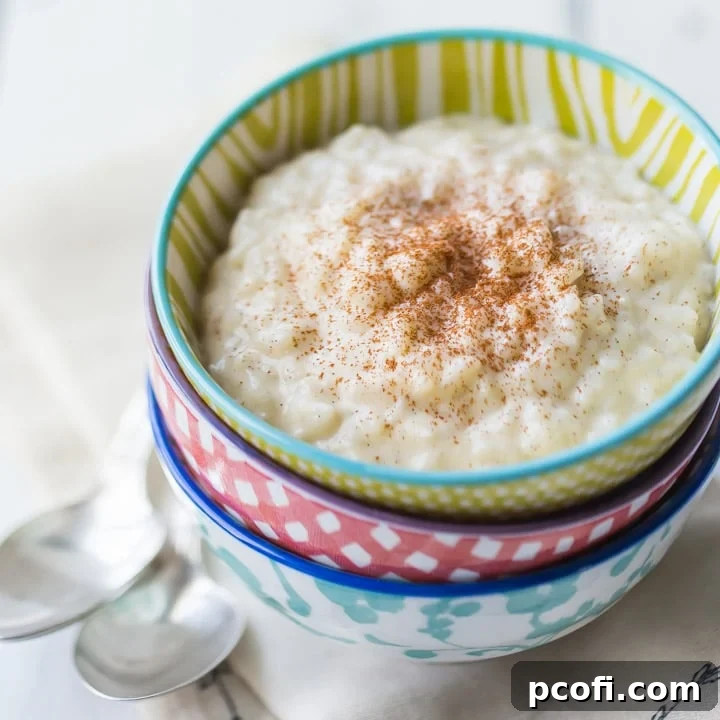 Three vibrantly colored bowls, stacked on a linen napkin, filled with creamy rice pudding and generously sprinkled with cinnamon.