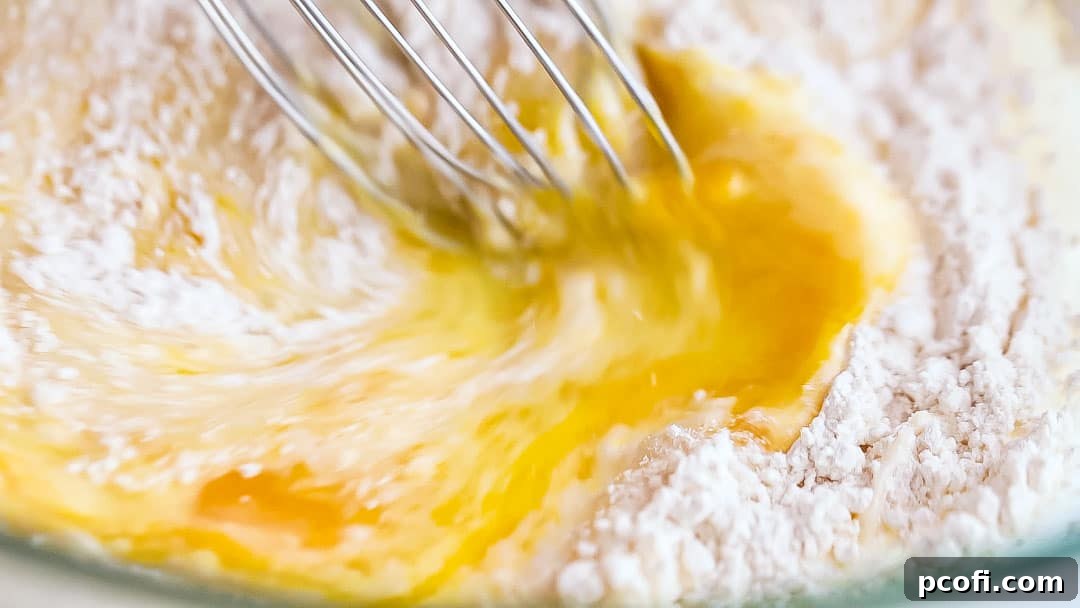 Whisking lemon pudding cake batter in a bowl to ensure smoothness.