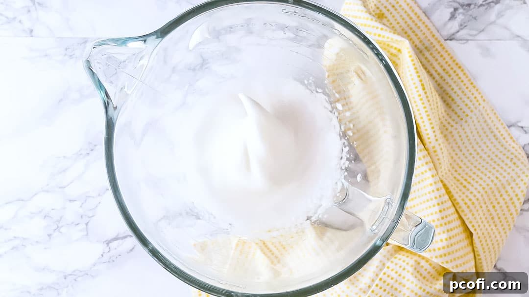 Stiffly whipped egg whites in a large glass mixing bowl, forming perfect peaks.