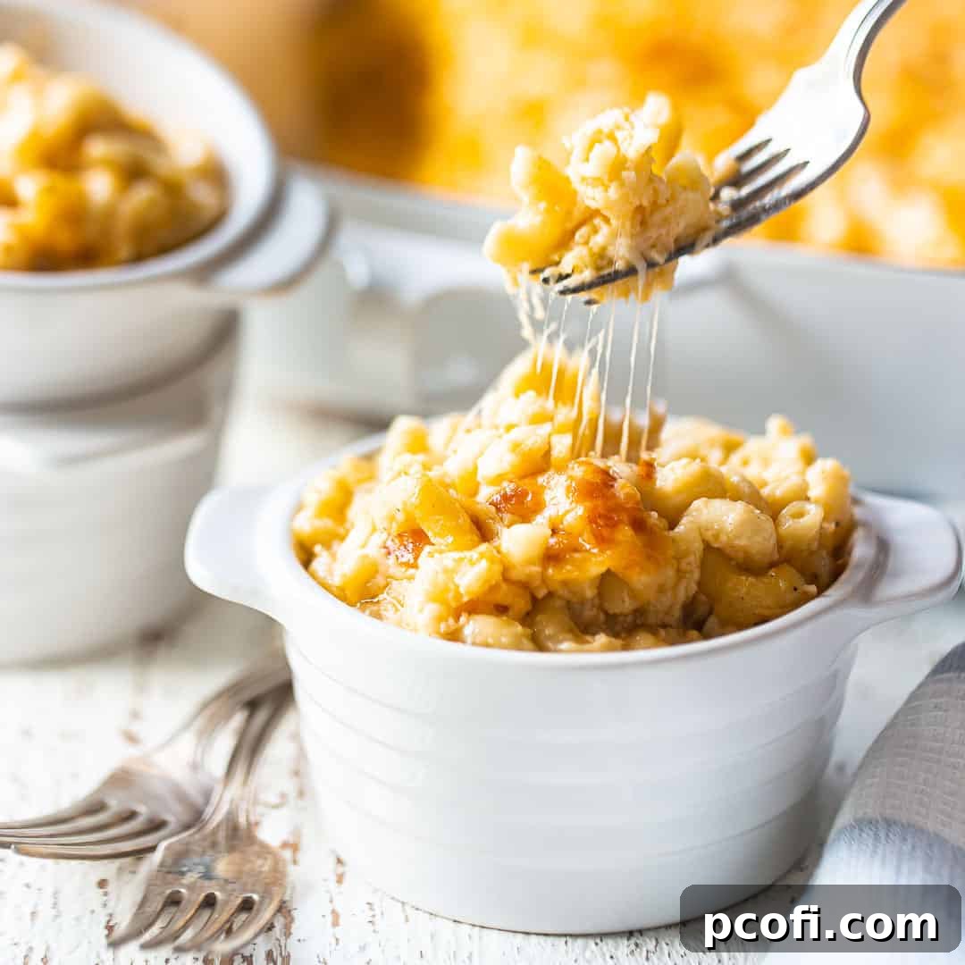 A fork pulling baked macaroni and cheese from an individual ramekin, showcasing its rich, gooey cheese pull.