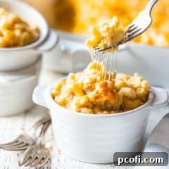 A fork pulling macaroni and cheese out of an individual ramekin, stretching the gooey cheese along with it.