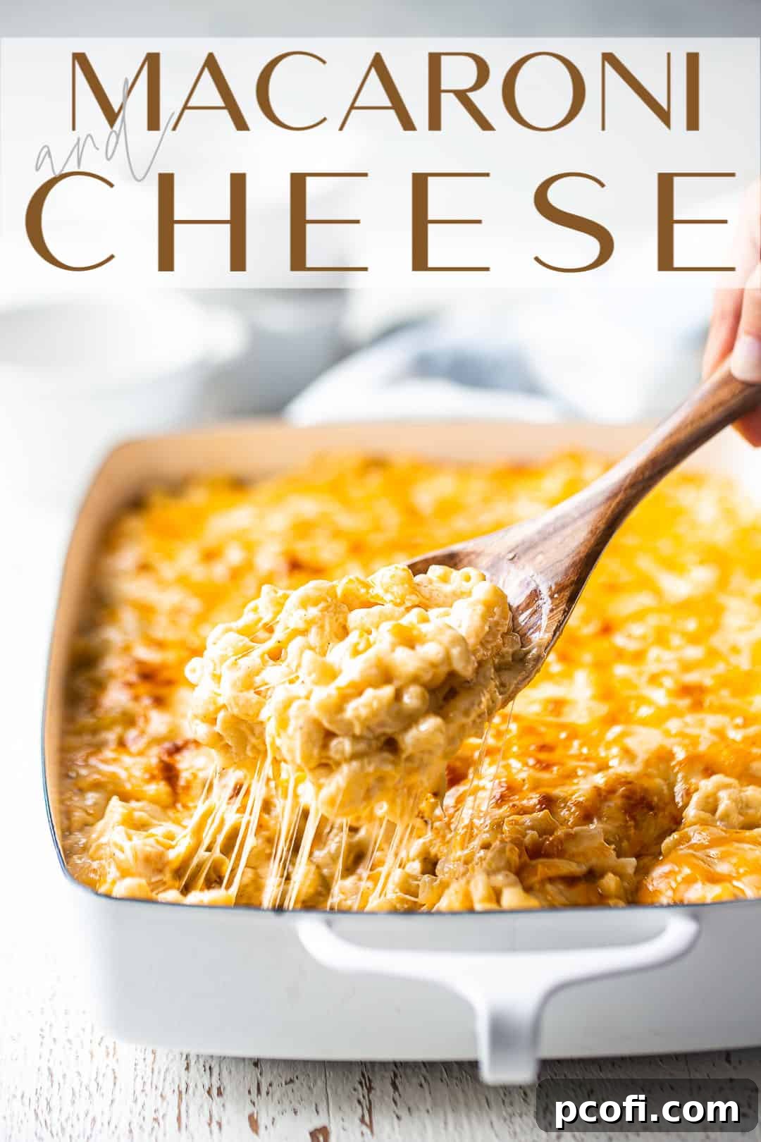 A serving spoon lifting a portion of unbelievably gooey, cheesy, and stretchy macaroni and cheese from a baking dish.