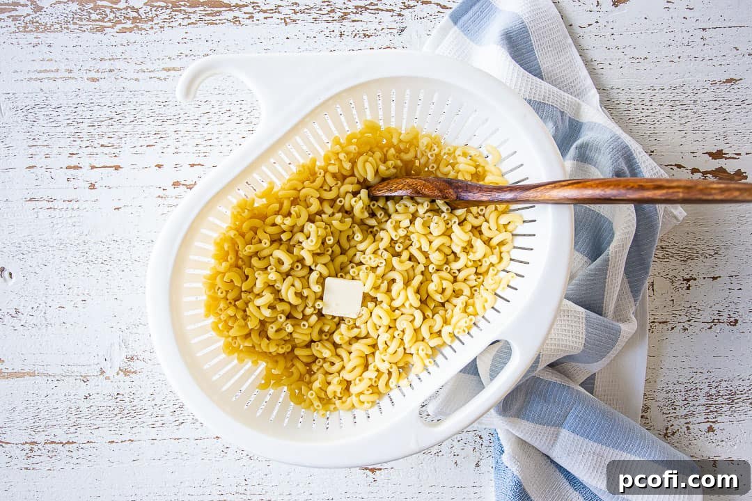 Freshly boiled elbow macaroni noodles tossed with butter in a large colander.