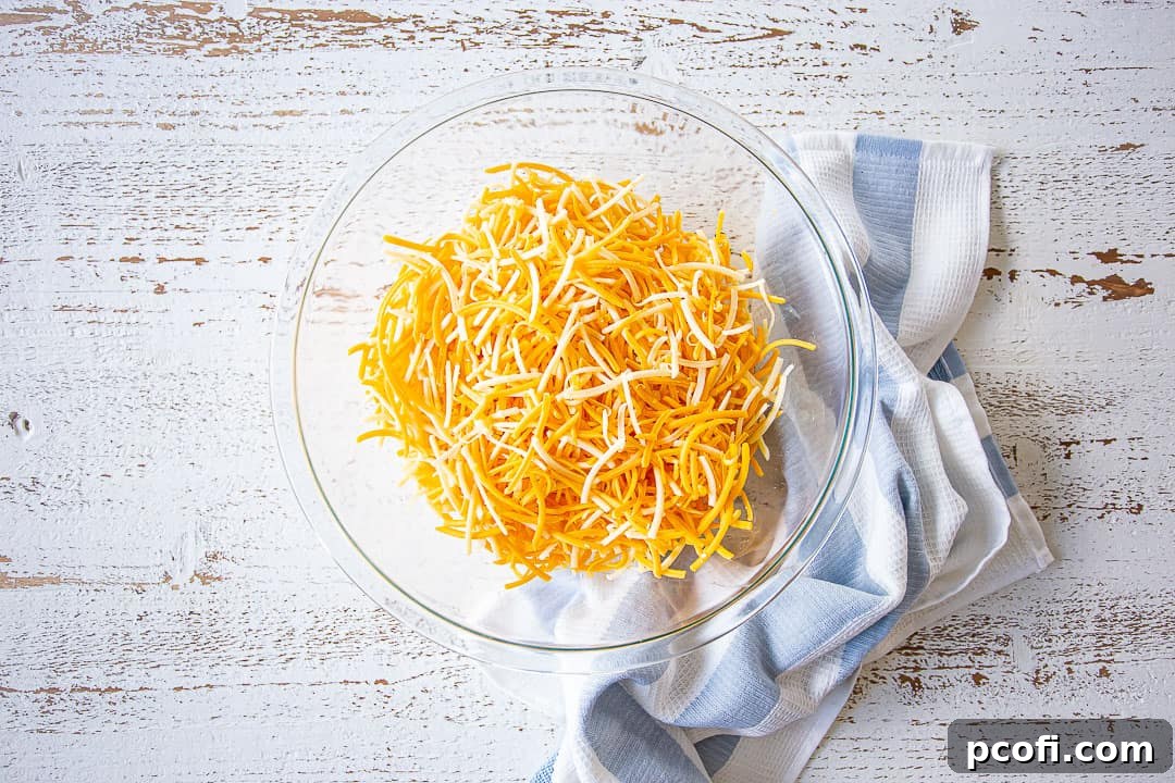 A generous pile of freshly shredded three-cheese blend (Cheddar, Gruyere, Mozzarella) in a large glass bowl.