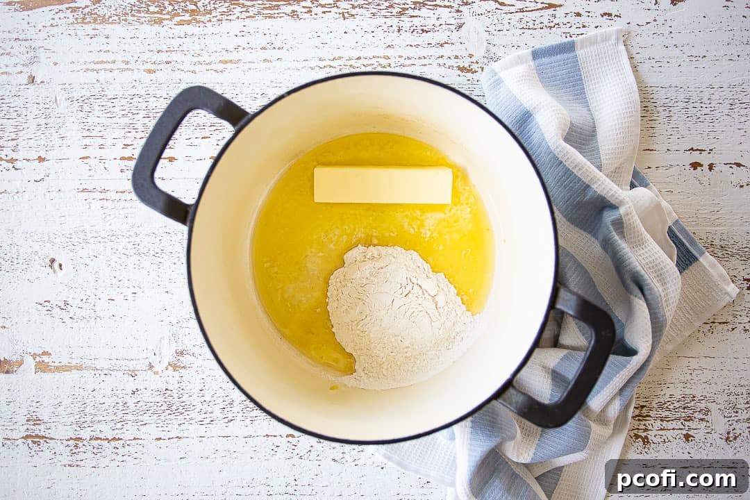 Close-up of butter melting in a large pot, with flour being stirred in to create a roux.