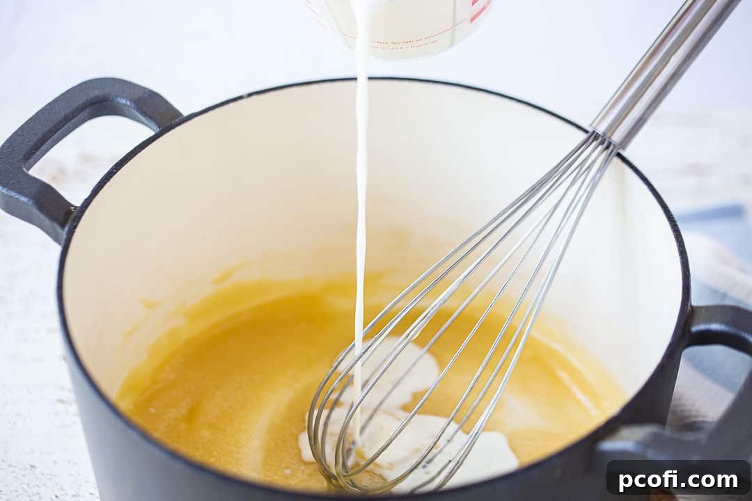Adding milk to a golden roux in a large pot, whisking to combine for the cream sauce.
