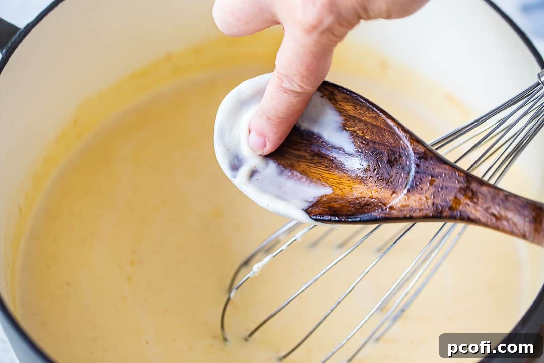 A thick, creamy béchamel sauce coating the back of a spoon, leaving a distinct trail when a finger is run through it.