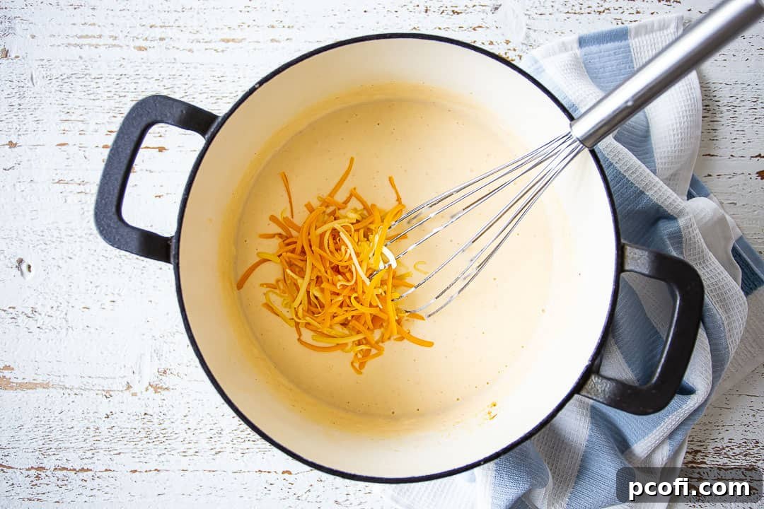 Shredded cheese being stirred into a thick, creamy béchamel sauce to create a Mornay sauce.
