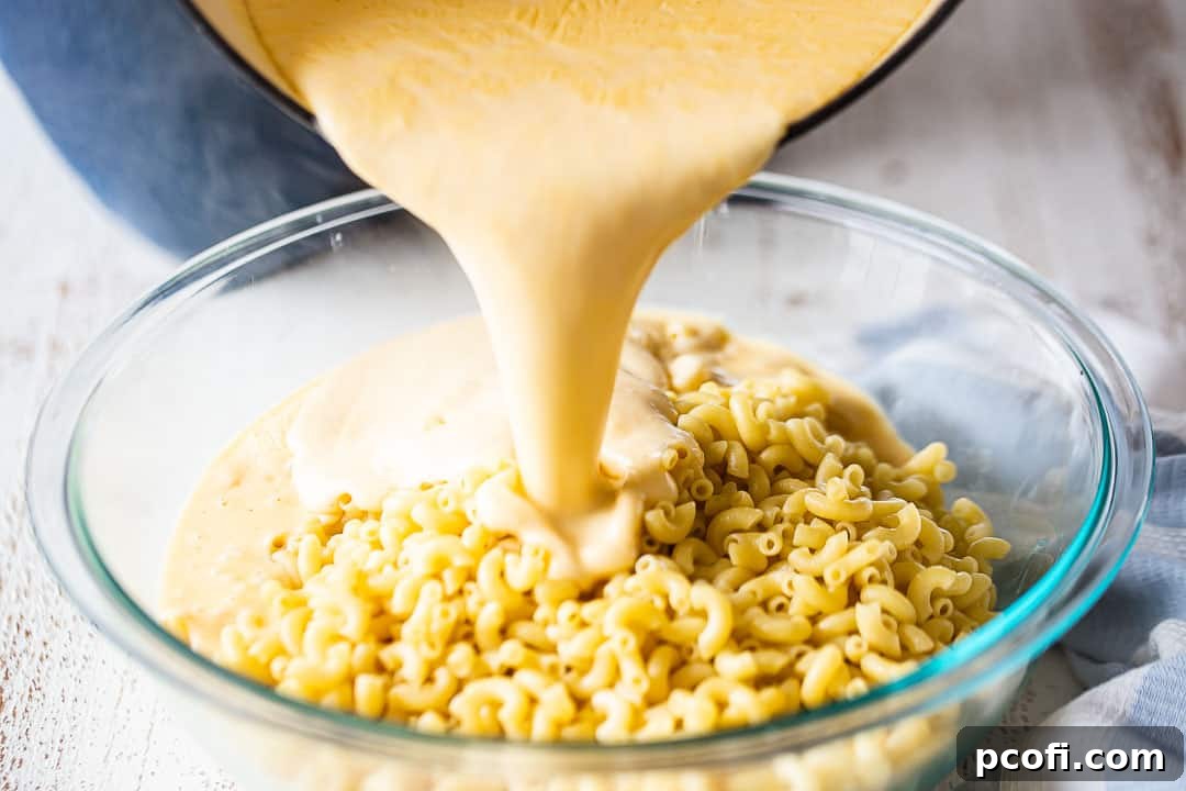 Pouring the rich, creamy cheese sauce over cooked elbow macaroni noodles in a large pot.