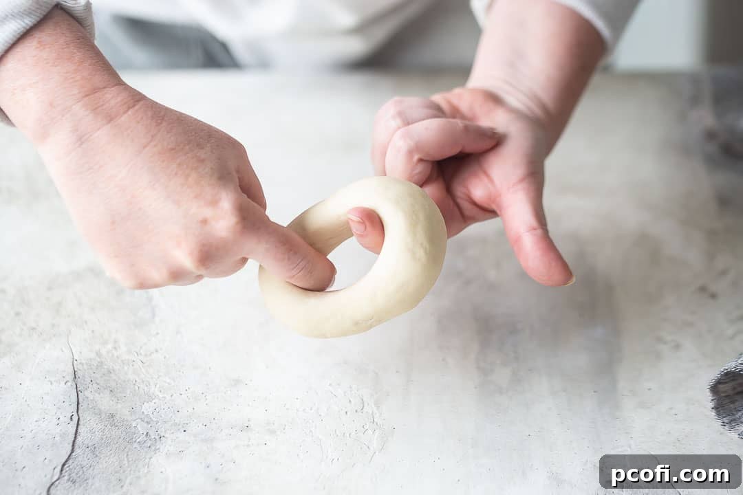 Hands shaping homemade bagels by stretching the center hole.
