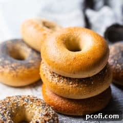 A selection of freshly baked bagels, including plain, poppy seed, sesame seed, and everything bagels, served on a newspaper.