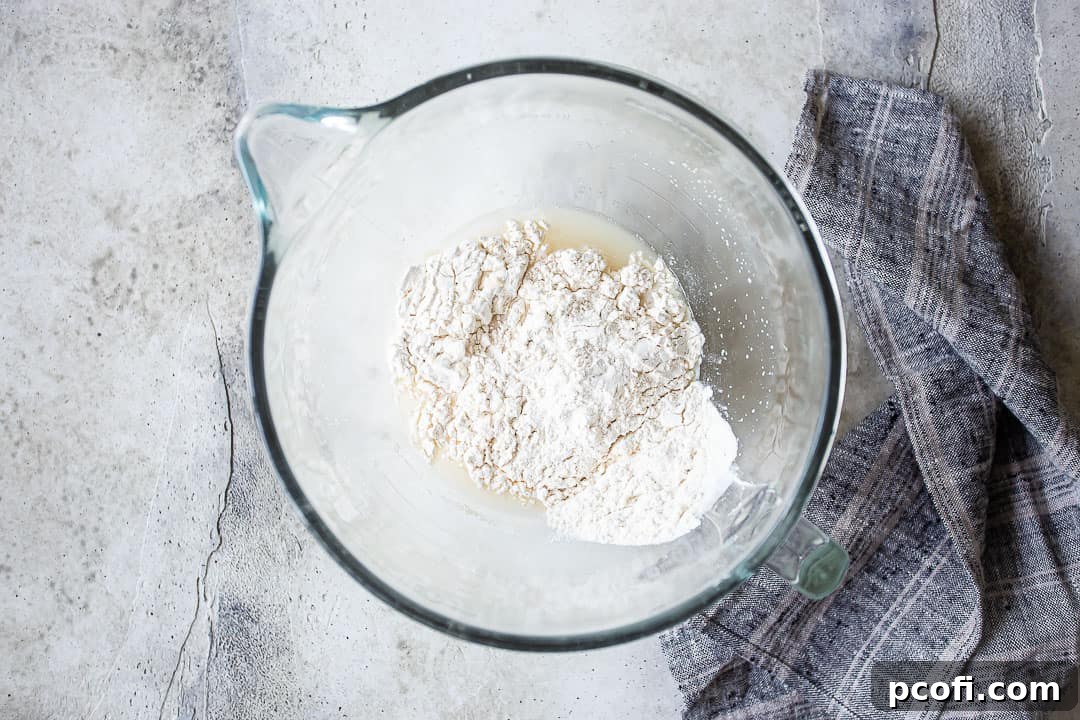 Adding all-purpose flour into a mixing bowl for the bagel dough preparation.