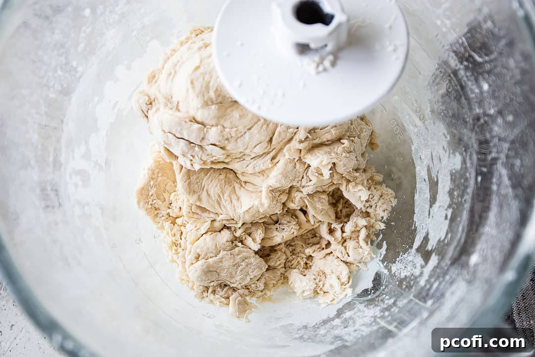 Mixing shaggy bagel dough with a dough hook attachment in a stand mixer.