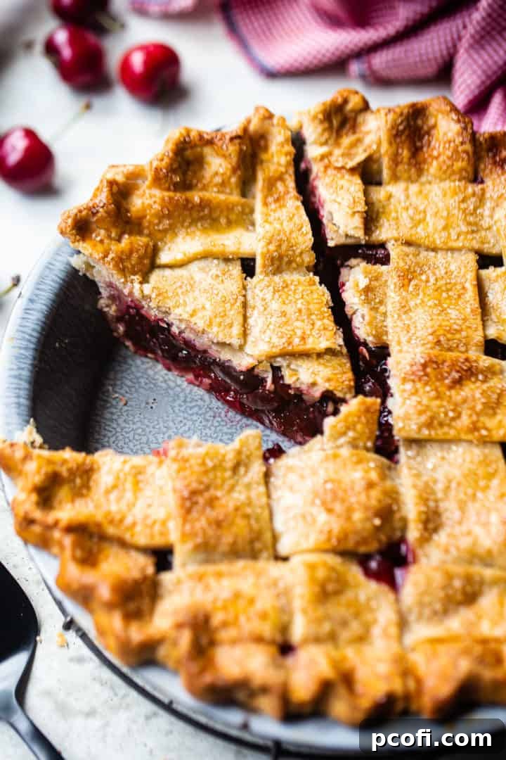 Best cherry pie recipe, freshly baked in a vintage pie dish, with a slice taken out to reveal the rich filling, set against a backdrop of fresh cherries and a rustic red checked cloth.