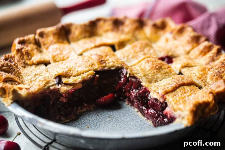 A delectable sweet cherry pie, freshly baked in a metal tin, with slices removed to showcase the magnificent layers of flaky pie crust and generously chunky fruit filling.