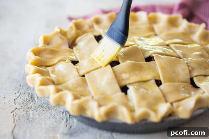 Brushing the top of a homemade cherry pie crust with an egg wash to achieve a golden-brown, glossy finish after baking.