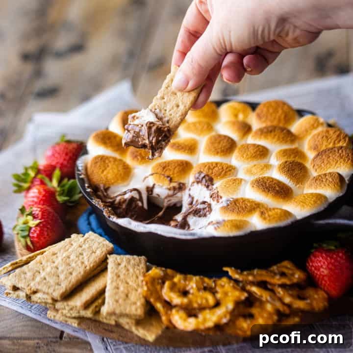 Dipping a graham cracker into s'mores dip baked in a skillet.