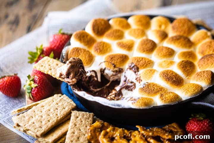S'mores dip made in the oven with in a skillet, surrounded by various dippers.