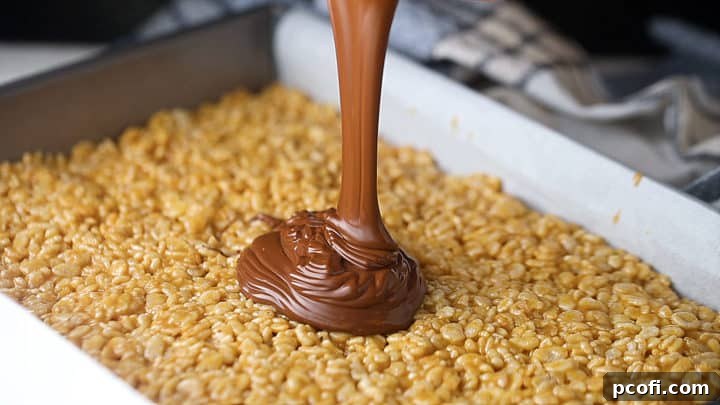 Pouring chocolate topping over scotcheroos, ready to be spread evenly.