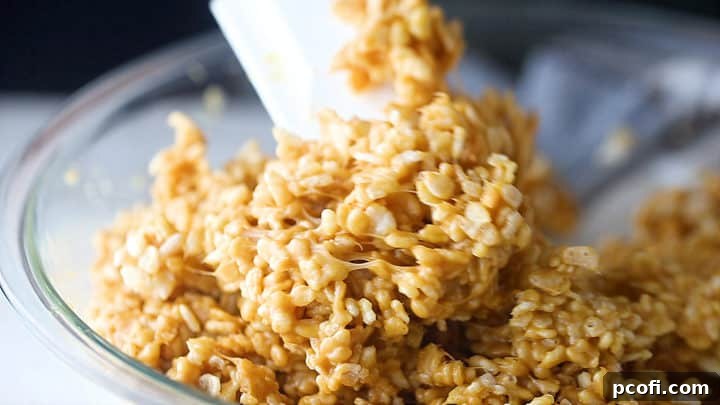 Stirring up scotcheroos with a silicone spatula, showing the cereal being evenly coated.