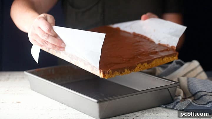 Removing cooled scotcheroos from the pan using parchment paper handles.